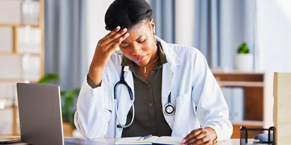 Médica com a mão direita na testa em feição preocupada