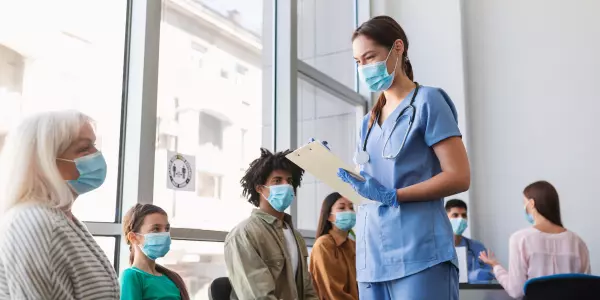 Profissional da saúde que não atende via teleconsulta de pé em sala lotada de pacientes.