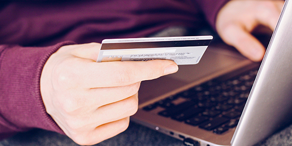 Pessoa com cartão de crédito na mão realiza pagamento online no computador