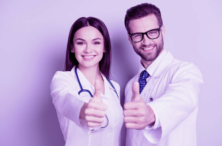 Médica e médico de jaleco branco sorriem e fazem sinal de positivo com o polegar, transmitindo confiança na gestão de planos de saúde