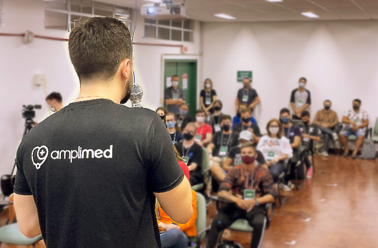 Homem de camiseta Amplimed fala ao microfone para plateia de estudantes na Semana Academica de Ciencia da Computacao