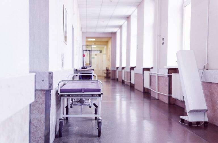 Corredor iluminado de hospital com maca hospitalar encostada na parede, representando impactos da guerra na saude mundial