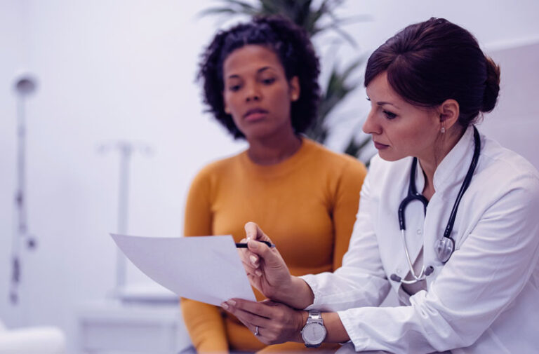 Medica de jaleco explicando resultado em papel para paciente atenta durante consulta no consultorio