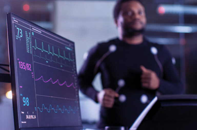 Monitor exibindo eletrocardiograma e pressao arterial enquanto homem com sensores faz avaliacao de medicina preventiva