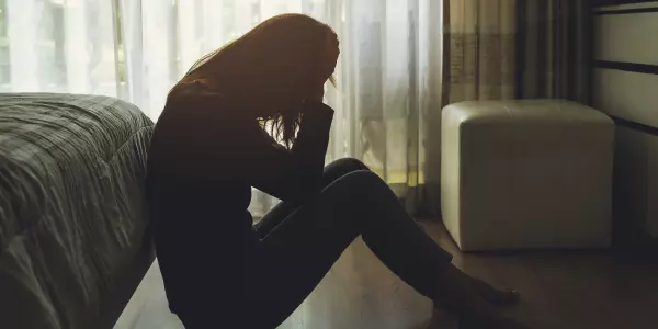 Mulher de perfil em ambiente escuro, sentada no chão, com as mãos no rosto