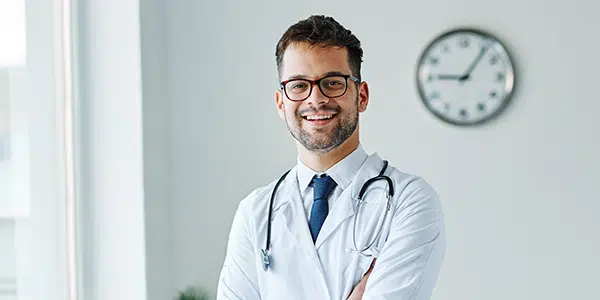 Médico com braços cruzados e estetoscópio no pescoço sorri para a câmera