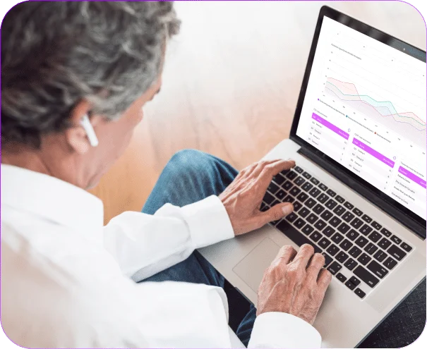 Pessoa de cabelos grisalhos usando notebook que exibe painel de gráficos e relatórios do sistema de gestão em saúde.